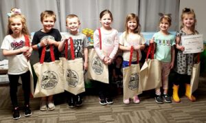 photo of Children holding book bags in library.