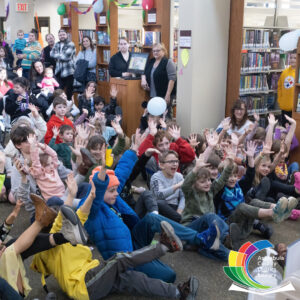 large group of children in library with hands raised.